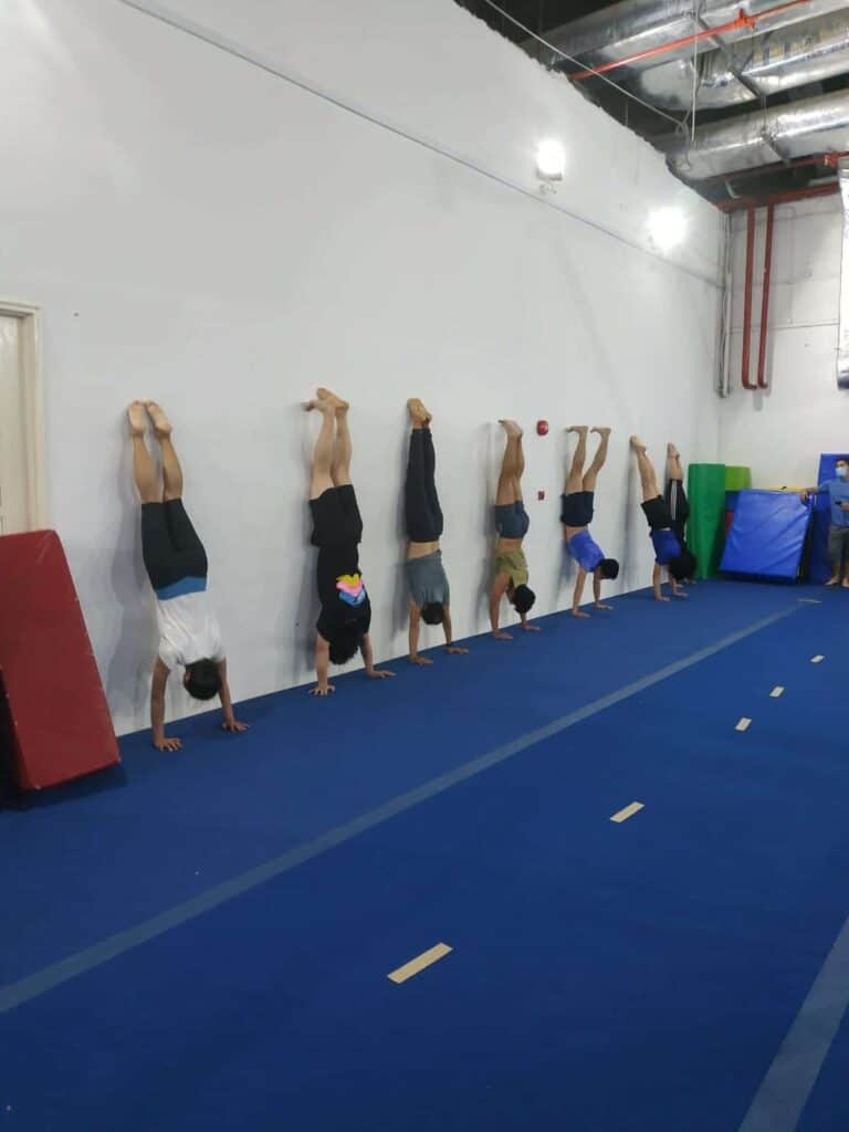 Children performing handstands against a wall during gymnastics class at Asia Gymnastics & Dance Academy.
